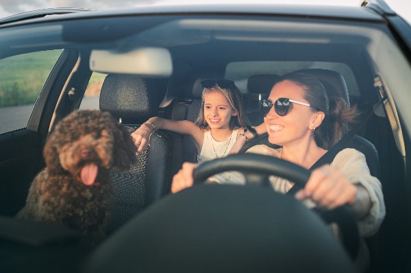 woman and child smiling in the car with dog sat next to them